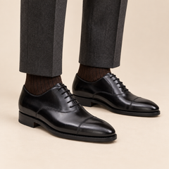 Black polished cap-toe Oxford shoes worn with charcoal tailored trousers