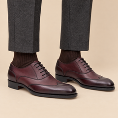Burgundy wingtip Oxford shoes with textured quarters on model